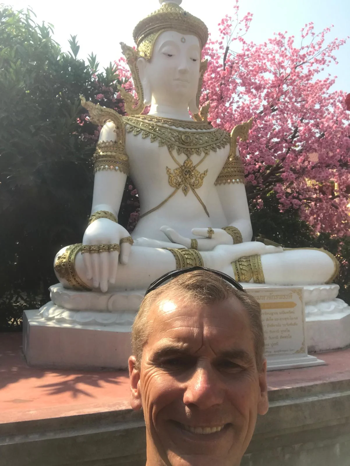 Mark Bell beside a white Buddha statue with cherry blossom behind