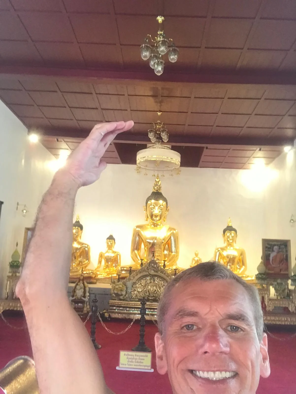 Mark Bell raising a hand before a row of golden Buddha statues